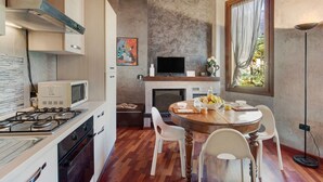 A compact kitchen with a gas stove, microwave, and oven, a dining table with chairs, a TV, and a window with curtains. - Holiday Home 'Wakesurfhouse 2' with Lake View, Private Terrace and Wi-Fi (Sulzano)