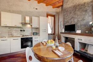 A modern kitchen with white cabinets, a round wooden table, and a fireplace.
