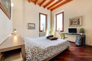 Une chambre à coucher avec un lit, un bureau avec un ordinateur, une chaise, une lampe et une fenêtre.