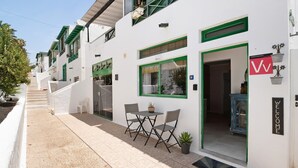 Un edificio blanco con detalles verdes, un letrero de bienvenida y una pequeña zona exterior con mesa y sillas.