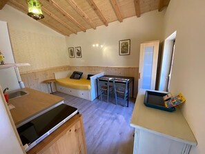 Quarto compacto com cozinha compacta, uma pequena mesa de jantar, um sofá e um espelho.