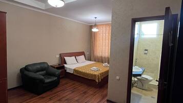 A room with a bed, a chair, a table, and a bathroom visible through an open door.