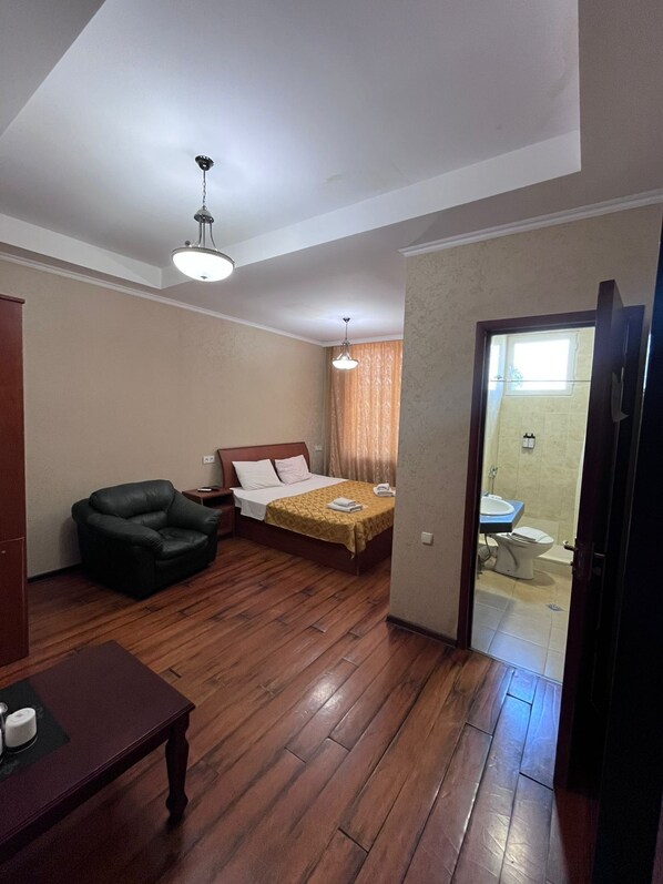 Een kamer met een bed, een stoel, een tafel en een badkamer zichtbaar door een open deur.