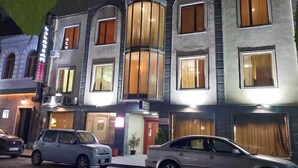 A multi-story hotel with a classic architectural design, featuring a central entrance with a sign, and two cars parked in front. - Aeetes Palace  (Kutaisi)