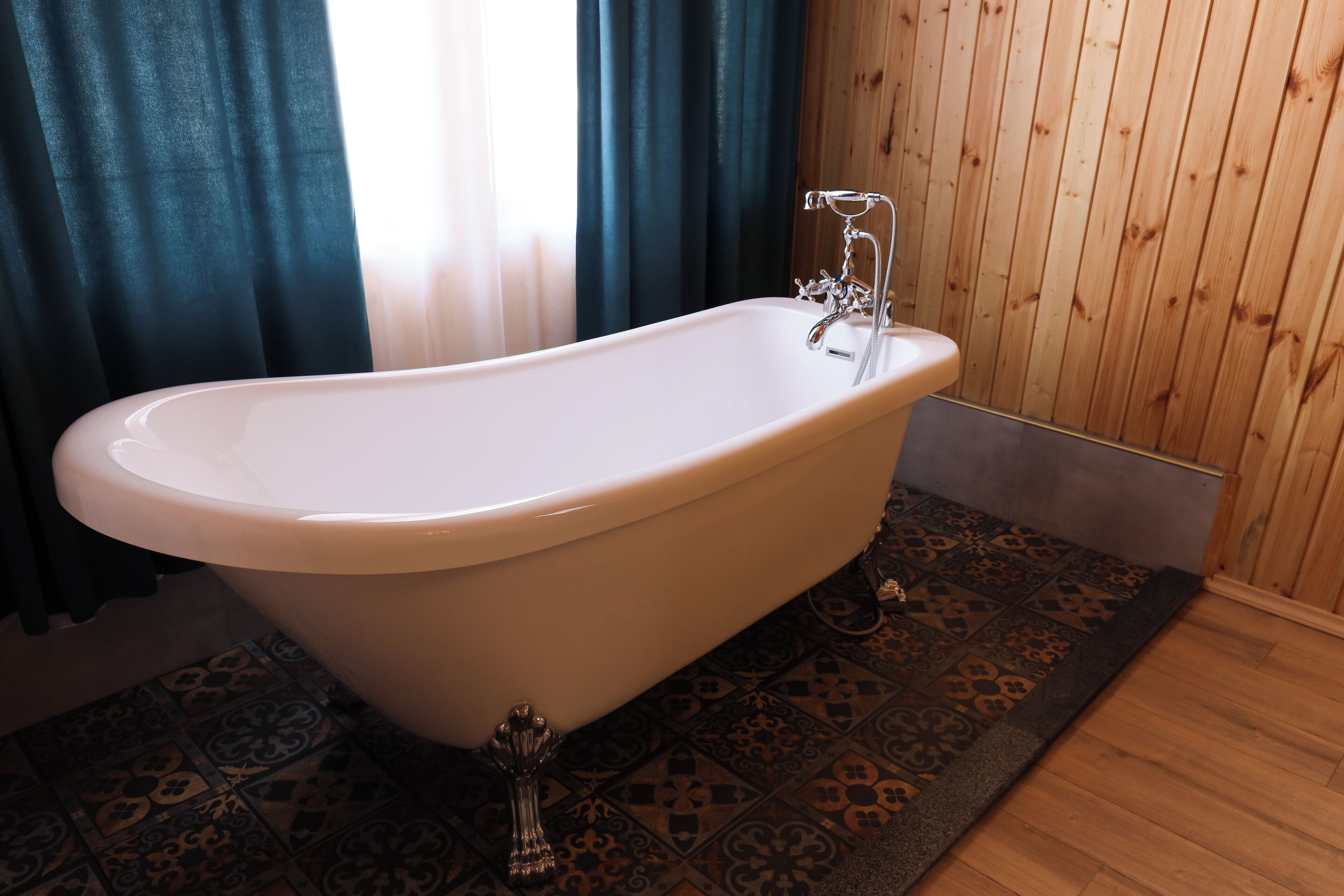 A freestanding bathtub in a bathroom with patterned tiles, wooden walls, and a dark rug.