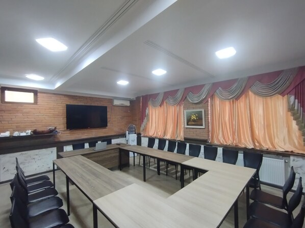 Una sala de conferencias con una larga mesa, sillas, una televisión y un muro de ladrillo.