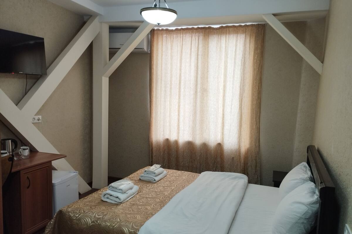 Ein Hotelzimmer mit Bett, Schreibtisch, Stuhl, Fernseher und einem Fenster mit Vorhängen.