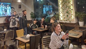 A cozy indoor seating area with tables and chairs, a TV screen displaying sports, and a decorative ceiling with plants. - Aeetes Palace  (Kutaisi)
