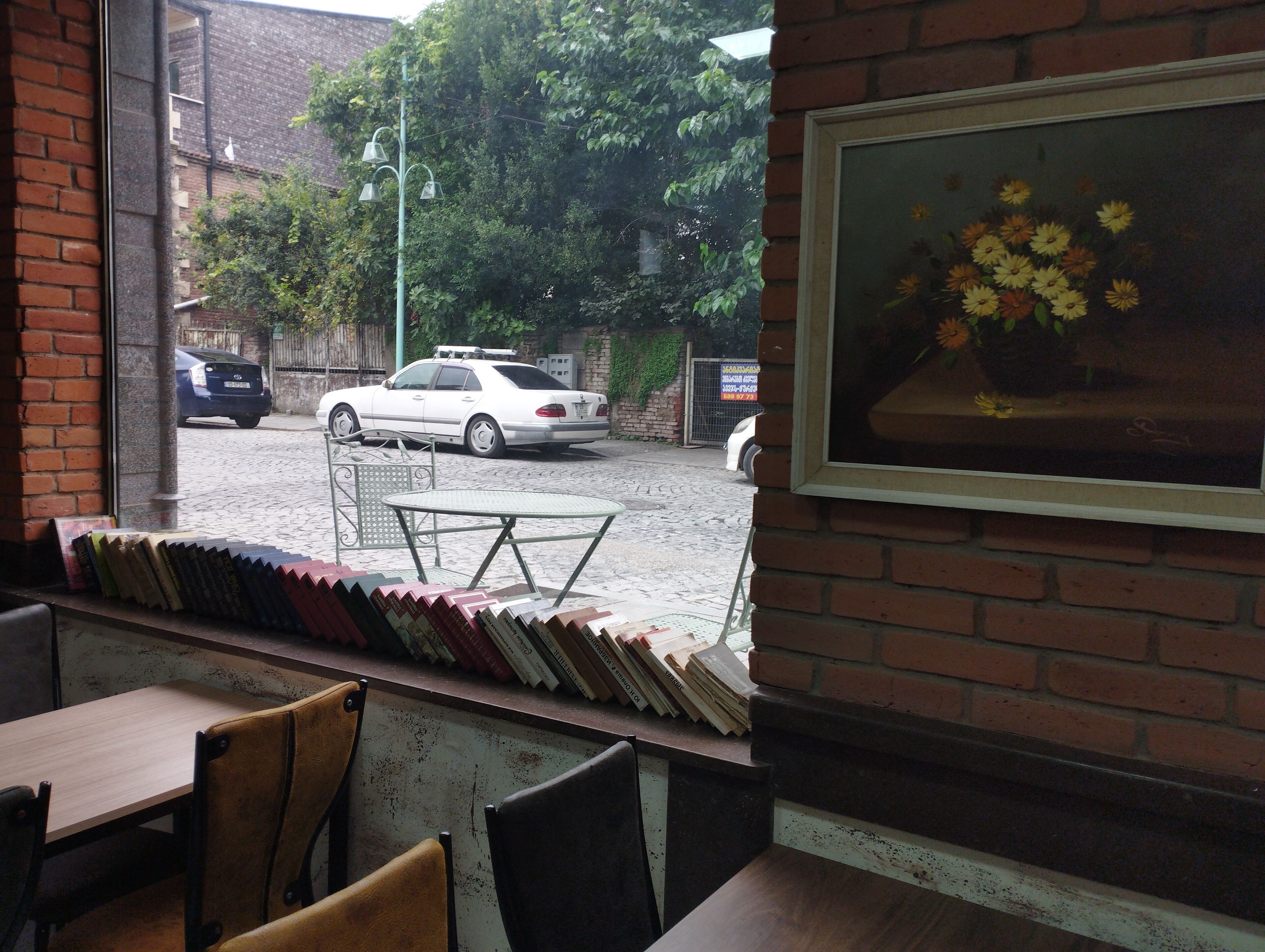 A view from a window with a brick wall, a table, chairs, and a framed picture of flowers.