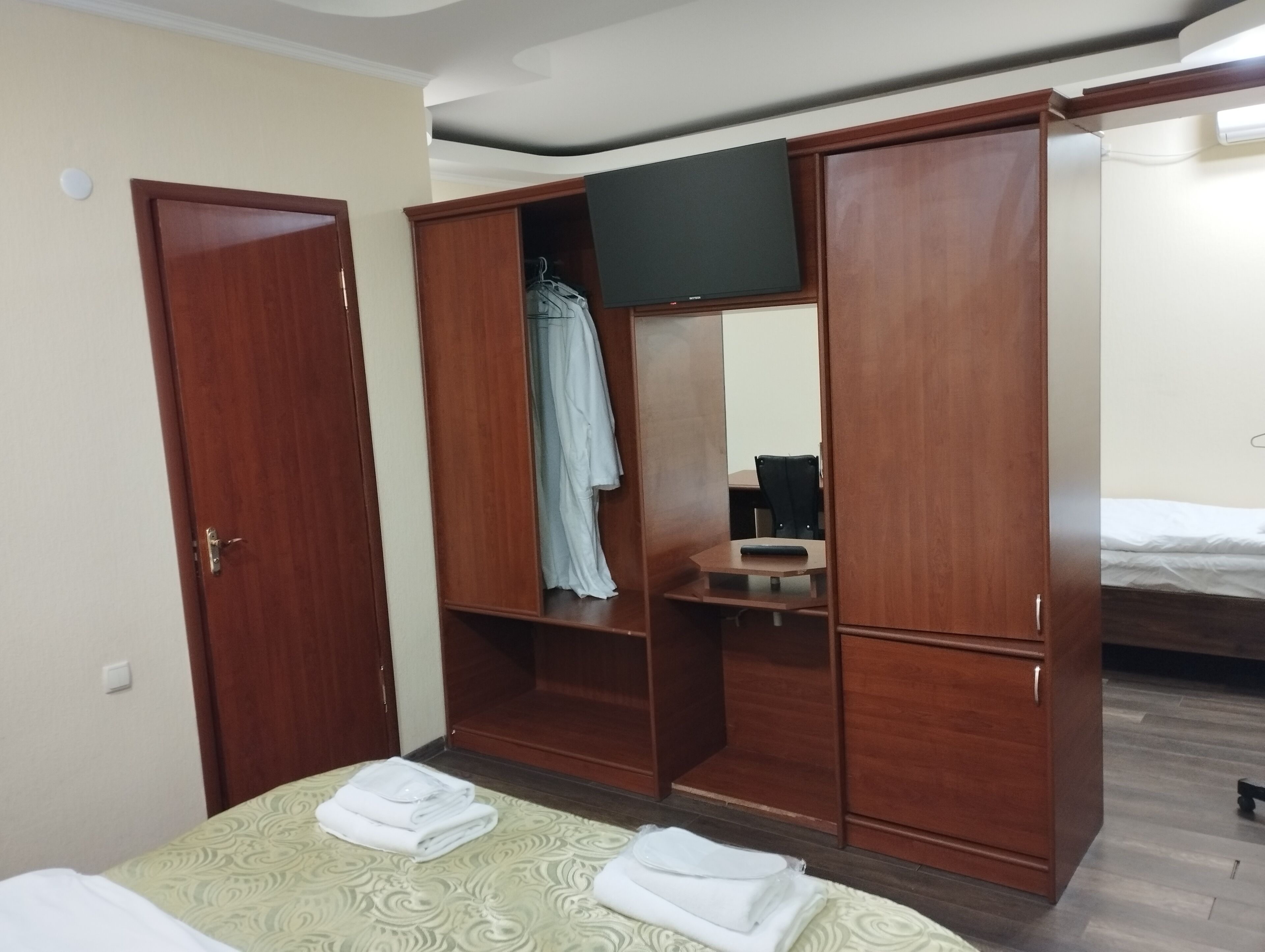 Una habitación de hotel con una cama, un armario con espejo, un escritorio con silla y un televisor.