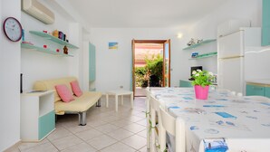 A compact living space with a kitchenette, a dining area, a sofa, and a small table with a potted plant. - Holiday Home 'Villa Bianca' with Terrace, Garden & Wi-Fi (San Teodoro)