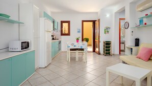 A compact kitchen with a microwave, refrigerator, and teal cabinets. There is a dining table with chairs and a small table with a pink pillow. - Holiday Home 'Villa Bianca' with Terrace, Garden & Wi-Fi (San Teodoro)