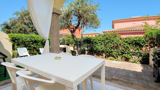 A patio with a white table and chairs, surrounded by greenery and a building with a tiled roof. - Holiday Home 'Villa Bianca' with Terrace, Garden & Wi-Fi (San Teodoro)