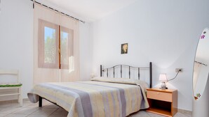 A bedroom with a bed, a nightstand, a chair, and a window with curtains. - Holiday Home 'Villa Bianca' with Terrace, Garden & Wi-Fi (San Teodoro)