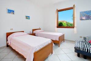 Une chambre avec deux lits simples, un petit canapé, une fenêtre donnant sur un paysage agréable et un mur orné de deux tableaux encadrés.