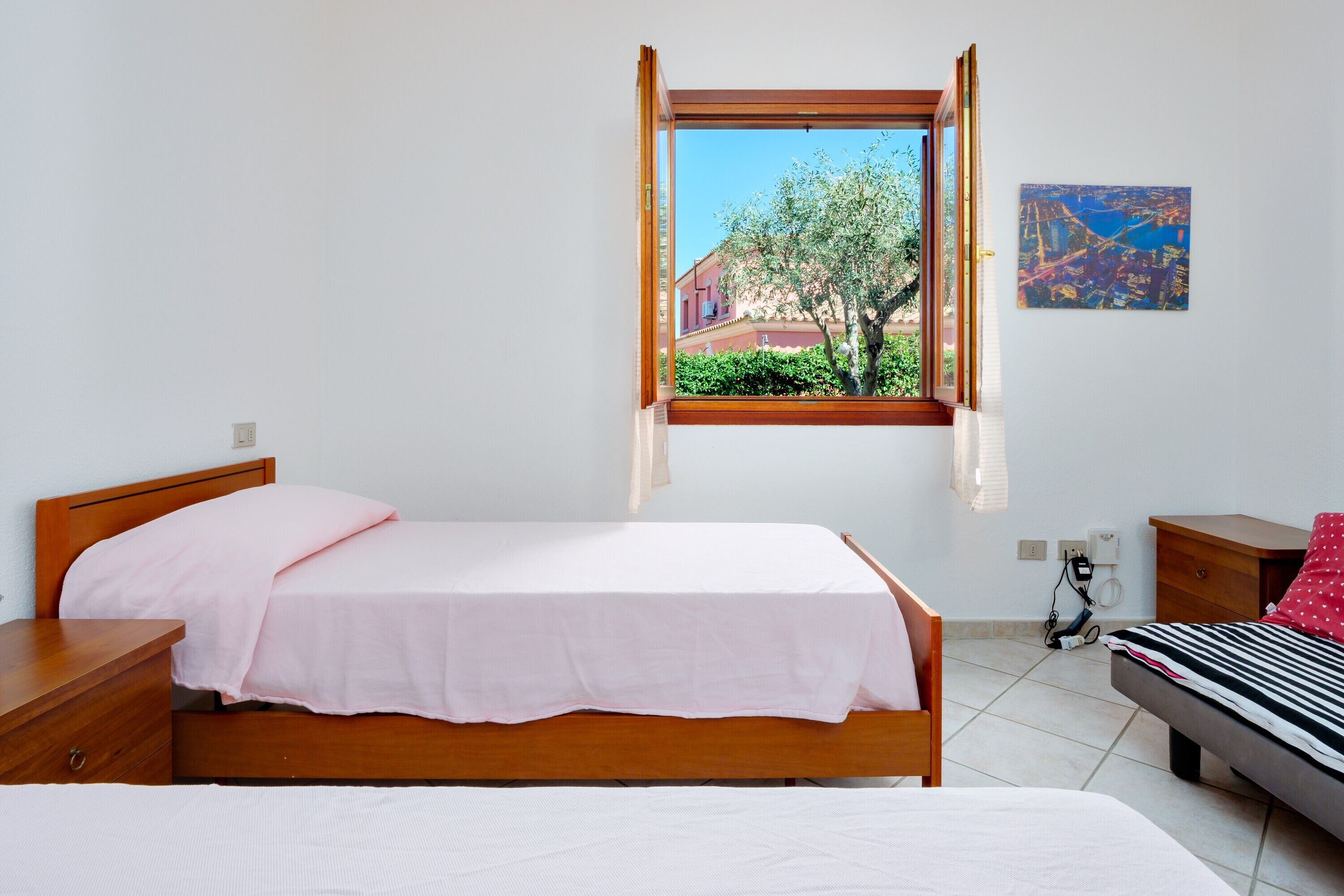 Een slaapkamer met een bed, een raam, een nachtkastje, een dressoir en een aan de muur hangend schilderij.