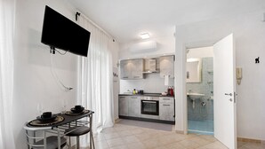 Eine moderne Küche mit Flachbildfernseher, eine Essecke mit Tisch und Stühlen sowie ein Badezimmer mit Waschbecken und Spiegel.