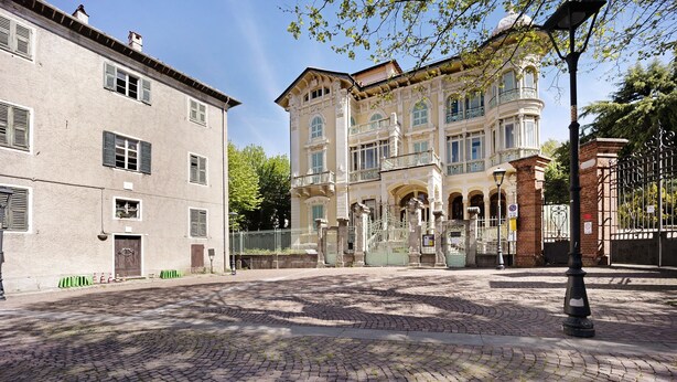 Eine Kopfsteinpflasterstraße mit historischen Gebäuden, einem schmiedeeisernen Tor und einem Laternenpfahl.