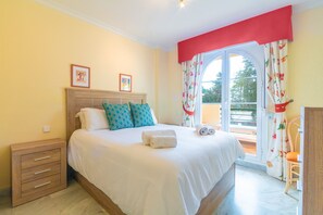 A bedroom with a bed, a nightstand, a window with curtains, and a view of the outside.