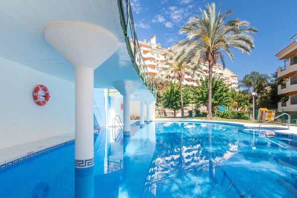 A swimming pool with a lifebuoy, palm trees, and a building in the background.