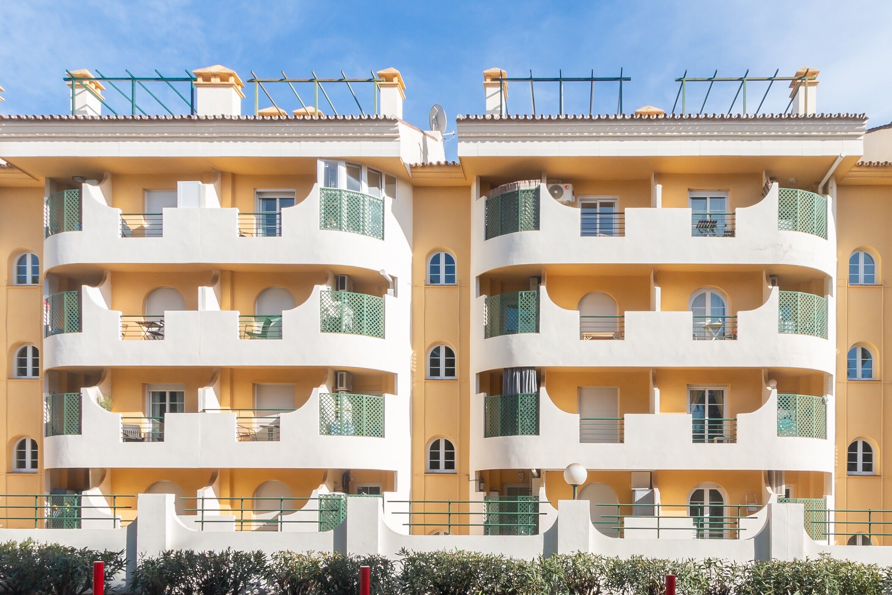 A symmetrical, multi-story building with balconies, a flat roof, and a clear sky.