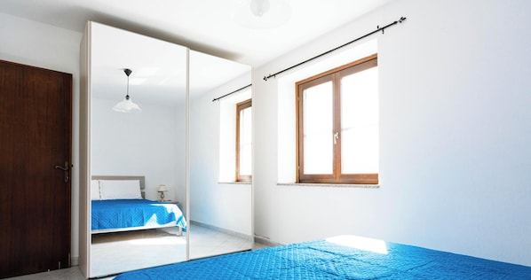 Un dormitorio con cama, armario, espejo, ventana y luz de techo.