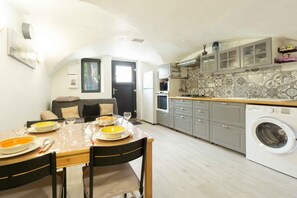 A compact kitchen with a washing machine, a dining table set with plates and cutlery, and a sofa in the adjacent living area.