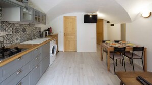 A compact kitchen with a washing machine, a dining area with a table set for four, and a TV mounted on the wall. - Apartment 'Charmant 3 Etoiles' with Mountain View, Private Terrace and Wi-Fi (Courchevel)