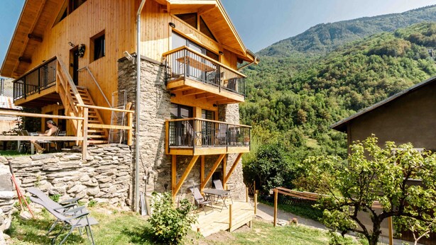 Un chalet en bois, avec une base en pierre, des balcons et une vue sur un paysage montagneux.