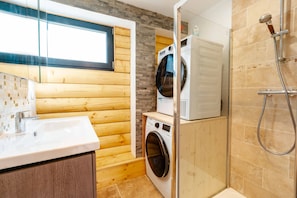 Une petite salle de bain avec un mur en bois, un lave-linge, une douche et un lavabo.