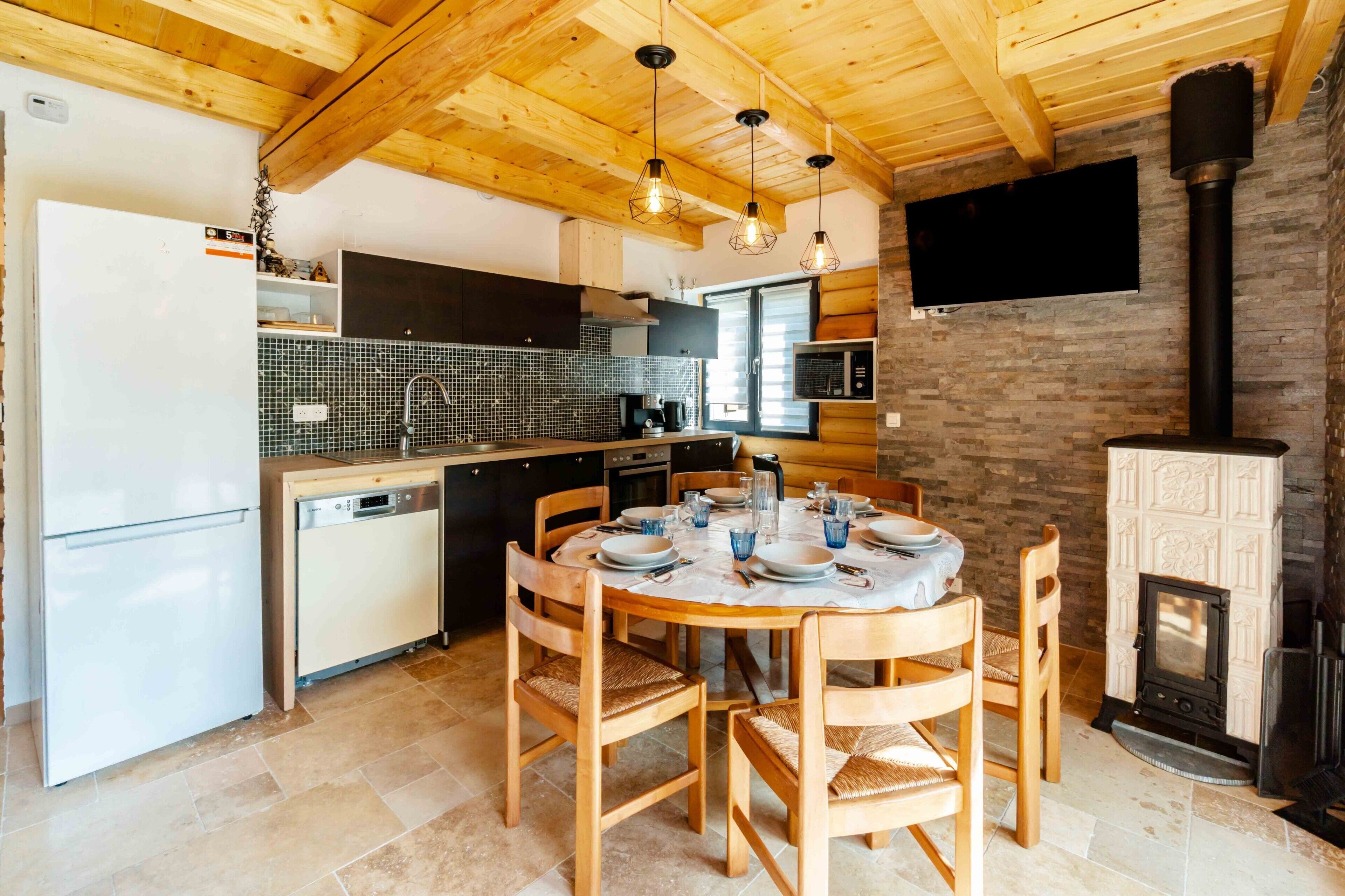 Een keuken met houten balken in het plafond, een eettafel gedekt voor vier personen, een inbouwoven en een open haard.