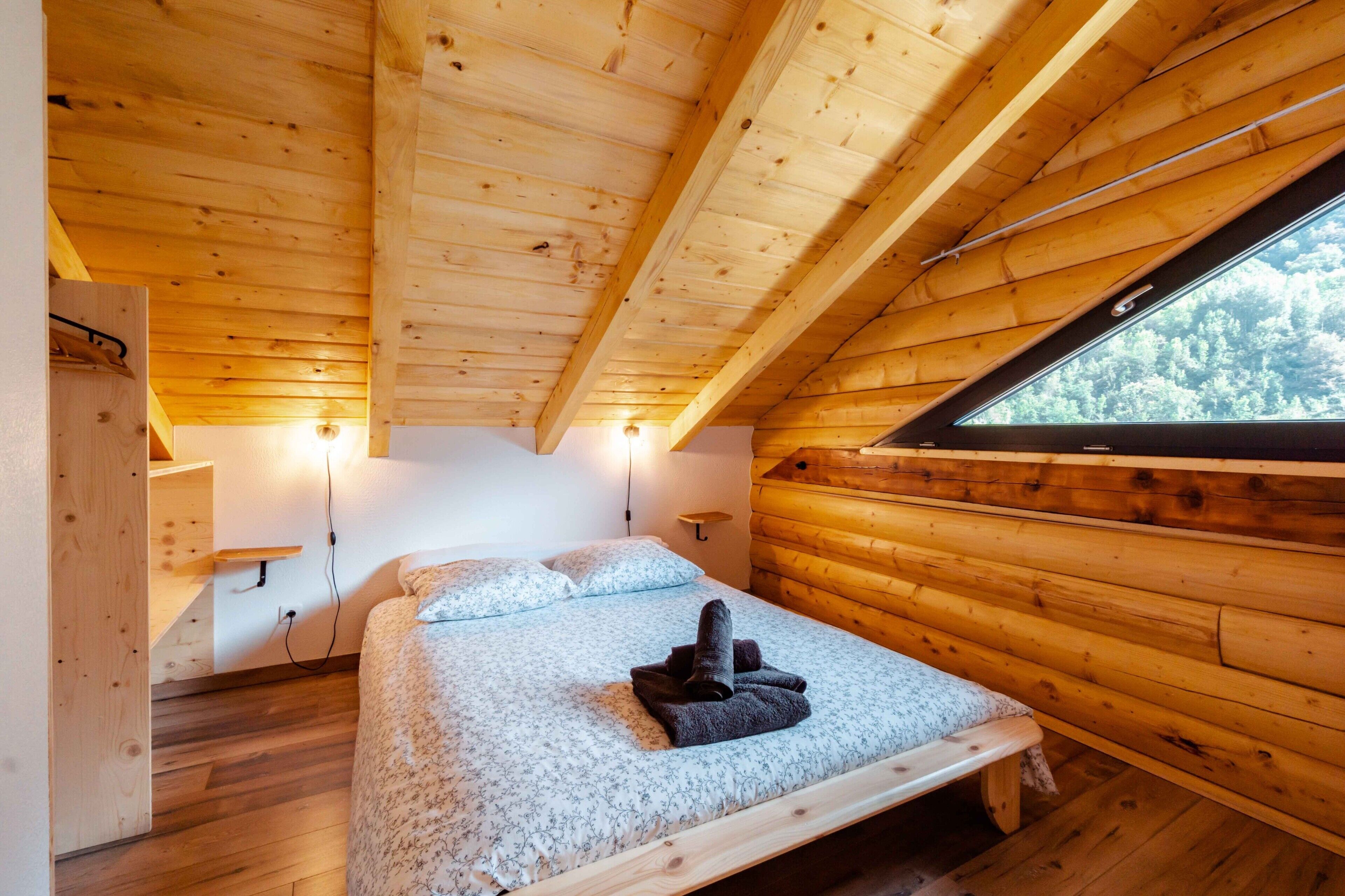 A wooden cabin bedroom with a bed, a bench, a window, and a shelf.