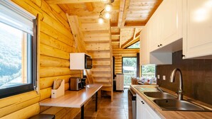 A wooden cabin interior with a kitchen area, a dining table, and a bench.