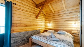 A wooden cabin room with a bed, stone wall, and wooden ceiling beams.