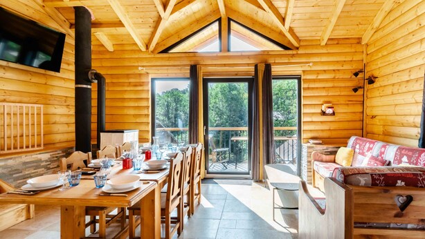 A wooden cabin with a dining area, a sofa, and a large window.