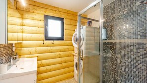 A bathroom with wooden walls, a glass shower enclosure, a sink, and a toilet.