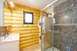 A bathroom with wooden walls, a glass shower enclosure, a sink, and a toilet.