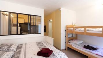 A room with a bunk bed, a single bed, and a kitchenette in the background.
