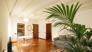 A spacious living room with a wooden floor, a grey sofa, a dining table with chairs, and a large potted plant. - Residenza Marconi 1 (Verona)
