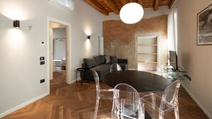 A modern living room with a wooden ceiling, a round dining table with clear chairs, a grey sofa, and a glass shelf unit. - Residenza Marconi 1 (Verona)