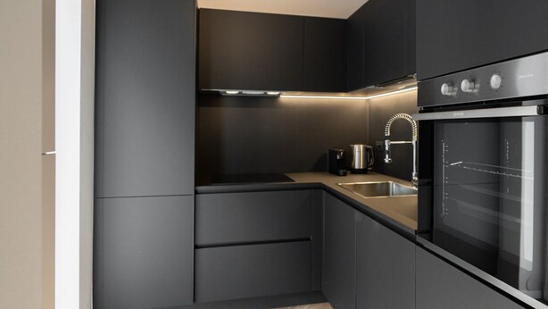 A modern kitchen with dark cabinetry, a built-in oven, and a herringbone wood floor. - Residenza Marconi 1 (Verona)
