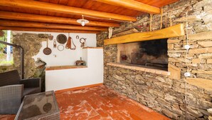 A rustic outdoor seating area with wicker furniture, a stone wall, and a wood-beamed ceiling. - Holiday Home "Casa Jerzu S'essia de su santu" with Sea View, Garden & Wi-Fi (Jerzu)
