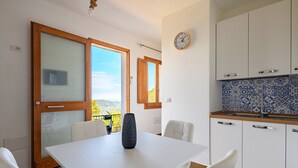A modern kitchen with white cabinets, a blue patterned backsplash, and a dining area with a white table and chairs. - Holiday Home "Casa Jerzu S'essia de su santu" with Sea View, Garden & Wi-Fi (Jerzu)