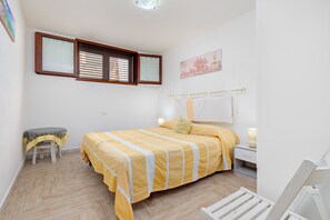 Ein Schlafzimmer mit Bett, Schreibtisch, Stuhl, Fenster und einem an der Wand befestigten Regal.
