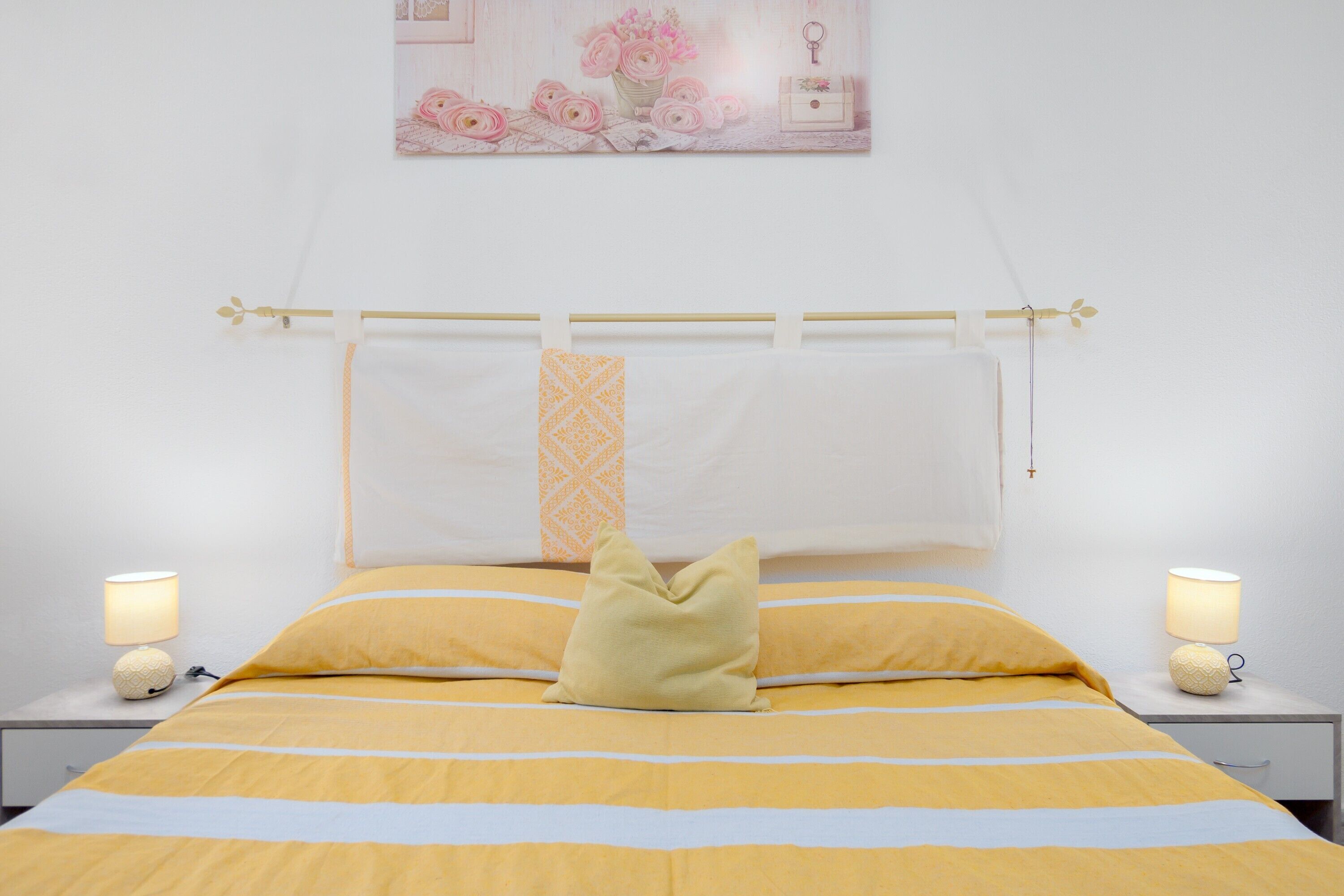 Ein Bett mit einer gelb-weißen Streifenbettdecke, einem Kopfkissen und einem Nachttisch mit Lampe.