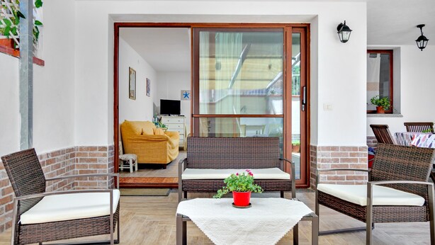 A room with wicker furniture, a red potted plant, and a sliding glass door leading to another room. - Holiday Apartment "Caterina" with Shared Terrace & Wi-Fi (Siniscola)