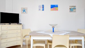 A room with a TV on a dresser, a dining table with chairs, and wall art. - Holiday Apartment "Caterina" with Shared Terrace & Wi-Fi (Siniscola)