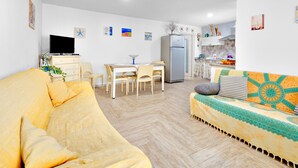 A living room with a sofa, a dining table with chairs, a TV, a refrigerator, and a kitchen area. - Holiday Apartment "Caterina" with Shared Terrace & Wi-Fi (Siniscola)