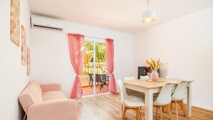 A room with a sofa, dining table with chairs, a TV, and a sliding glass door leading to an outdoor area with a yellow structure. - "Gran Sol Family 1" Apartment with Shared Pool, Wi-Fi, and Air Conditioning (Tourist Tax Included) (Felanitx)
