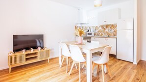 A modern kitchen with white cabinets, a wooden dining table with white chairs, a flat-screen TV, and a decorative backsplash. - "Gran Sol Family 1" Apartment with Shared Pool, Wi-Fi, and Air Conditioning (Tourist Tax Included) (Felanitx)